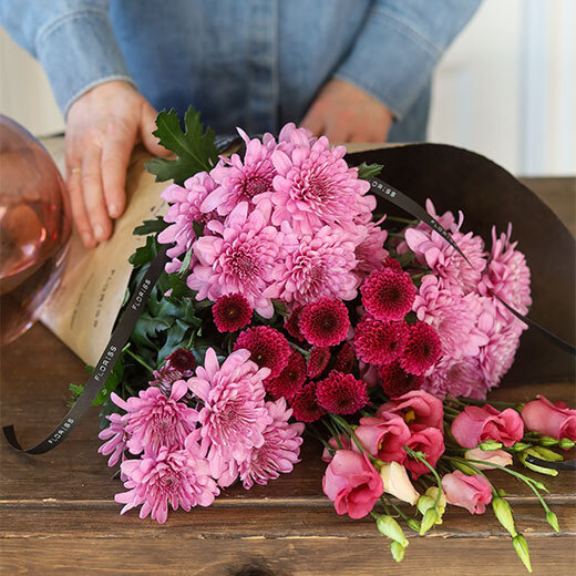En flott bukett med tre ulike blomster i rosa-toner innpakket i papir