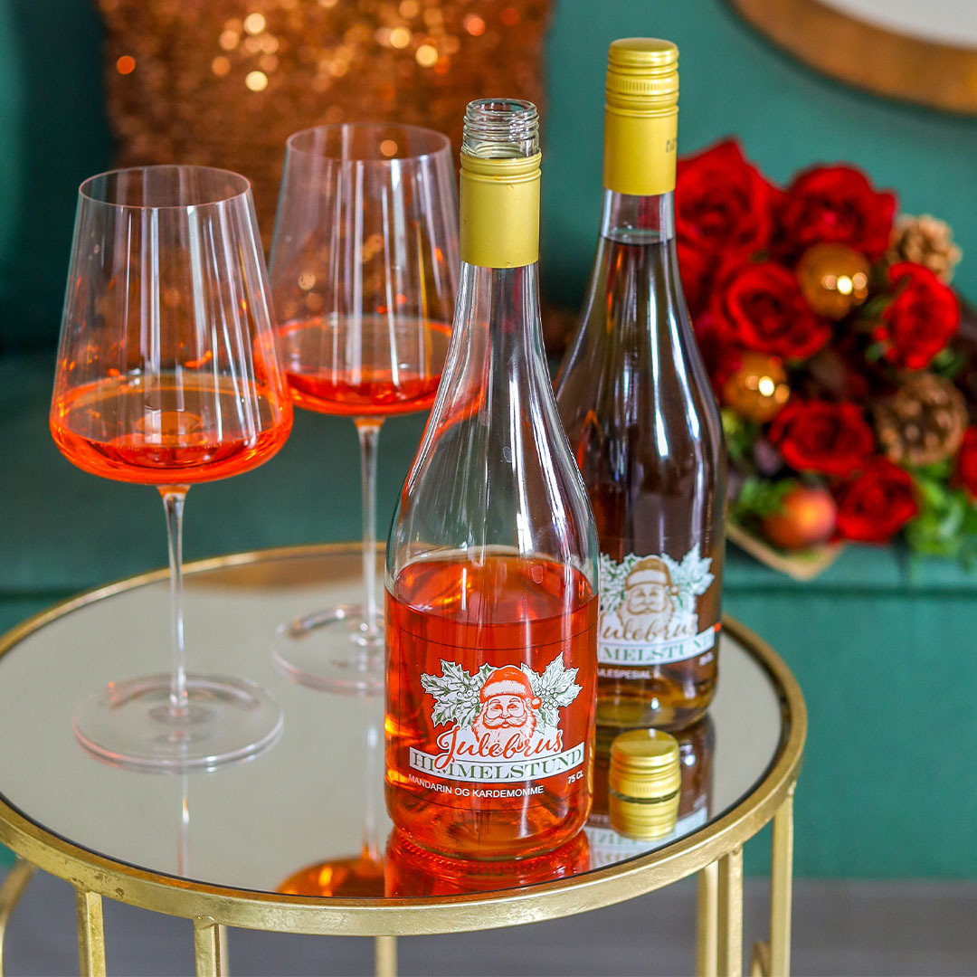 Julebrus Mandarin og Julebrus Spesial på et bord, to glass som er sjenket med Julebrus Mandarin og en julebukett i bakgrunnen